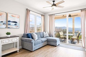 A living room with a gray sectional sofa, a white console table, and a large window with curtains. - Cozy 2-bedroom condo with beautiful views of Norris Lake (LaFollette)