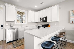 A modern kitchen with white cabinetry, a built-in microwave, and a central island with bar stools. - Cozy 2-bedroom condo with beautiful views of Norris Lake (LaFollette)