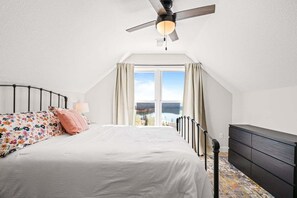Ein Schlafzimmer mit Bett, Schminktisch, Deckenventilator und einem Fenster mit Vorhängen.