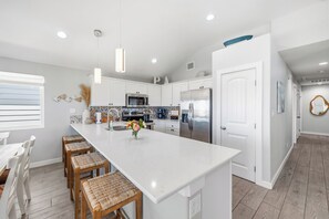 A modern kitchen with white cabinetry, a central island with bar stools, stainless steel appliances, and a decorative backsplash.