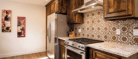 A kitchen with wooden cabinets, a stainless steel refrigerator, a gas stove, and patterned backsplash.