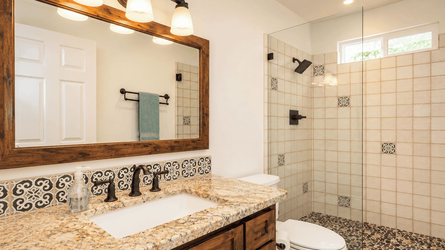 A bathroom with a marble countertop, a sink, a toilet, a shower with glass doors, and a mirror with lights.