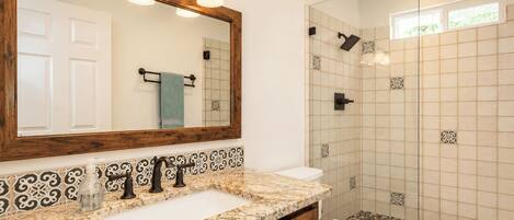 A bathroom with a marble countertop, a sink, a toilet, a shower with glass doors, and a mirror with lights.