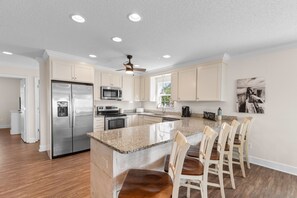 A modern kitchen with a central island, stainless steel appliances, and a ceiling fan. - Private Pool House — Surfside Beach SC · Sleeps 14, Walk to Beach (Surfside Beach)