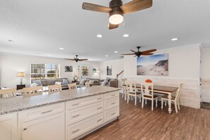A spacious kitchen with a large island, wooden dining table, and ceiling fans. - Private Pool House — Surfside Beach SC · Sleeps 14, Walk to Beach (Surfside Beach)