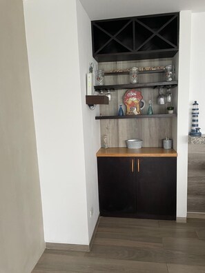 Ett kök med mörka skåp, en bänkskiva i trä och hyllor med glasburkar och köksredskap.
