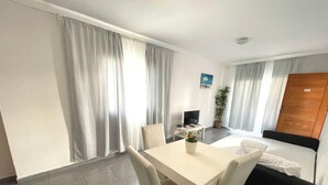 Habitación de hotel con cama, escritorio, silla, televisión, planta y ventana con cortinas.