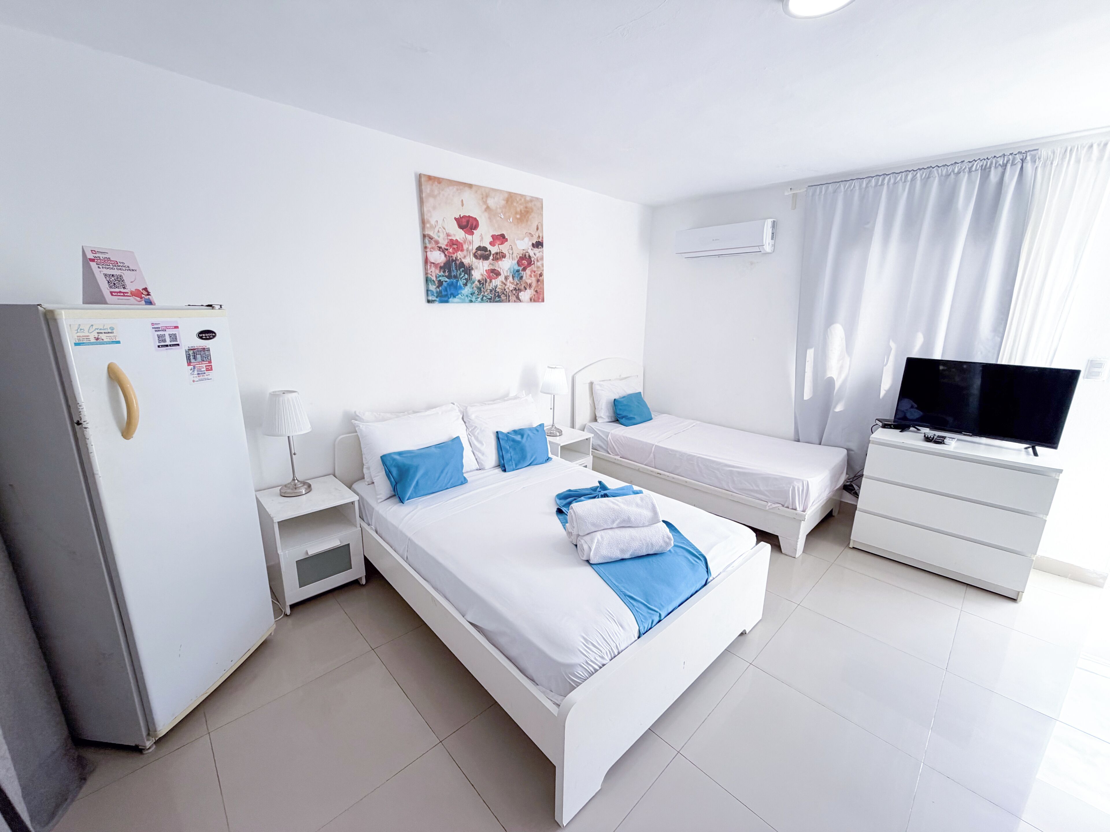 Ein Hotelzimmer mit Bett, Fernseher, Kühlschrank, Nachttisch und einem Bild an der Wand.