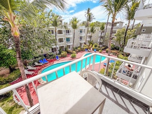 A hotel pool area with multiple levels of balconies, palm trees, and lounge chairs. - Tropical Adventure STUDIOS HOTEL & SPA (Punta Cana)