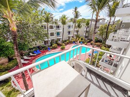 A hotel pool area with multiple levels of balconies, palm trees, and lounge chairs.