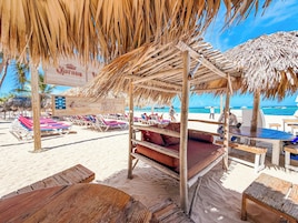 Una estructura de madera frente a la playa con techo de paja, sillas de descanso y un cartel que indica una tienda de regalos.