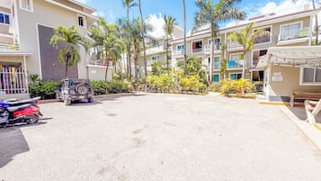 Un hotel de varios pisos con estacionamiento, palmeras y un jeep.