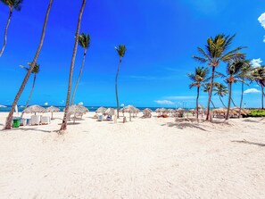 Uma praia com palmeiras, guarda-sóis de palha e espreguiçadeiras.