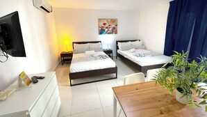 Habitación de hotel con dos camas, un escritorio, una silla, televisor, un cuadro y una planta en maceta.