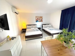 A hotel room with two beds, a desk, a chair, a TV, a painting, and a potted plant. - Tropical Adventure STUDIOS HOTEL & SPA (Punta Cana)