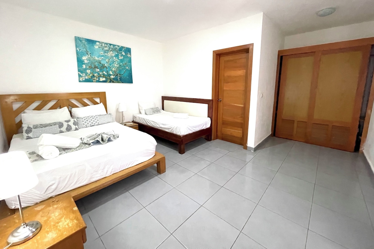 A hotel room with two beds, a wooden headboard, a painting on the wall, and a tiled floor.