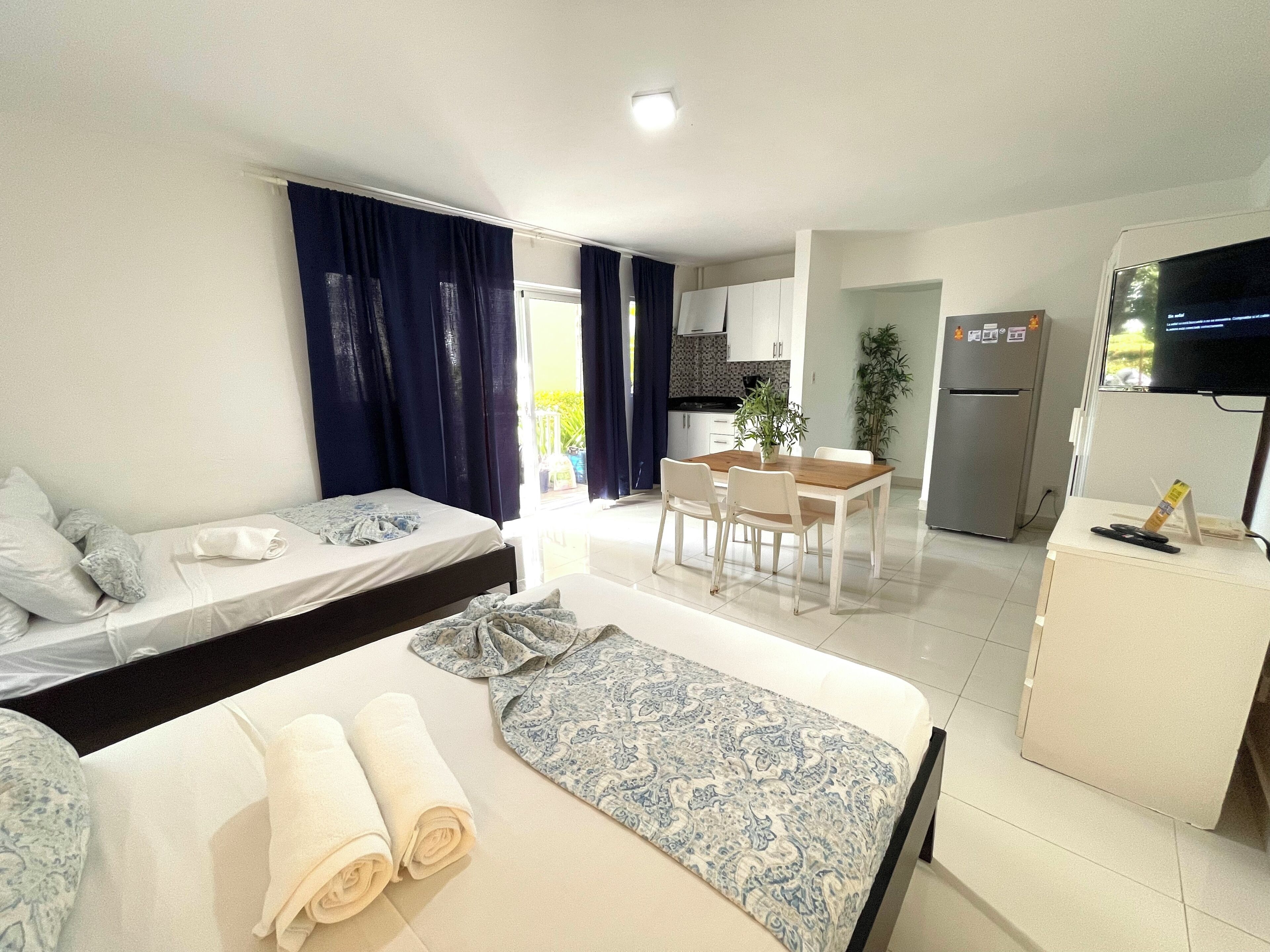 Una camera d'albergo con un letto, un divano, un tavolo da pranzo con sedie, un angolo cottura e una televisione.