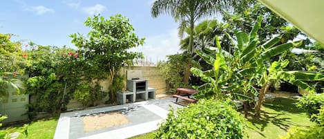 A backyard with a barbecue area, a paved patio, and lush greenery.