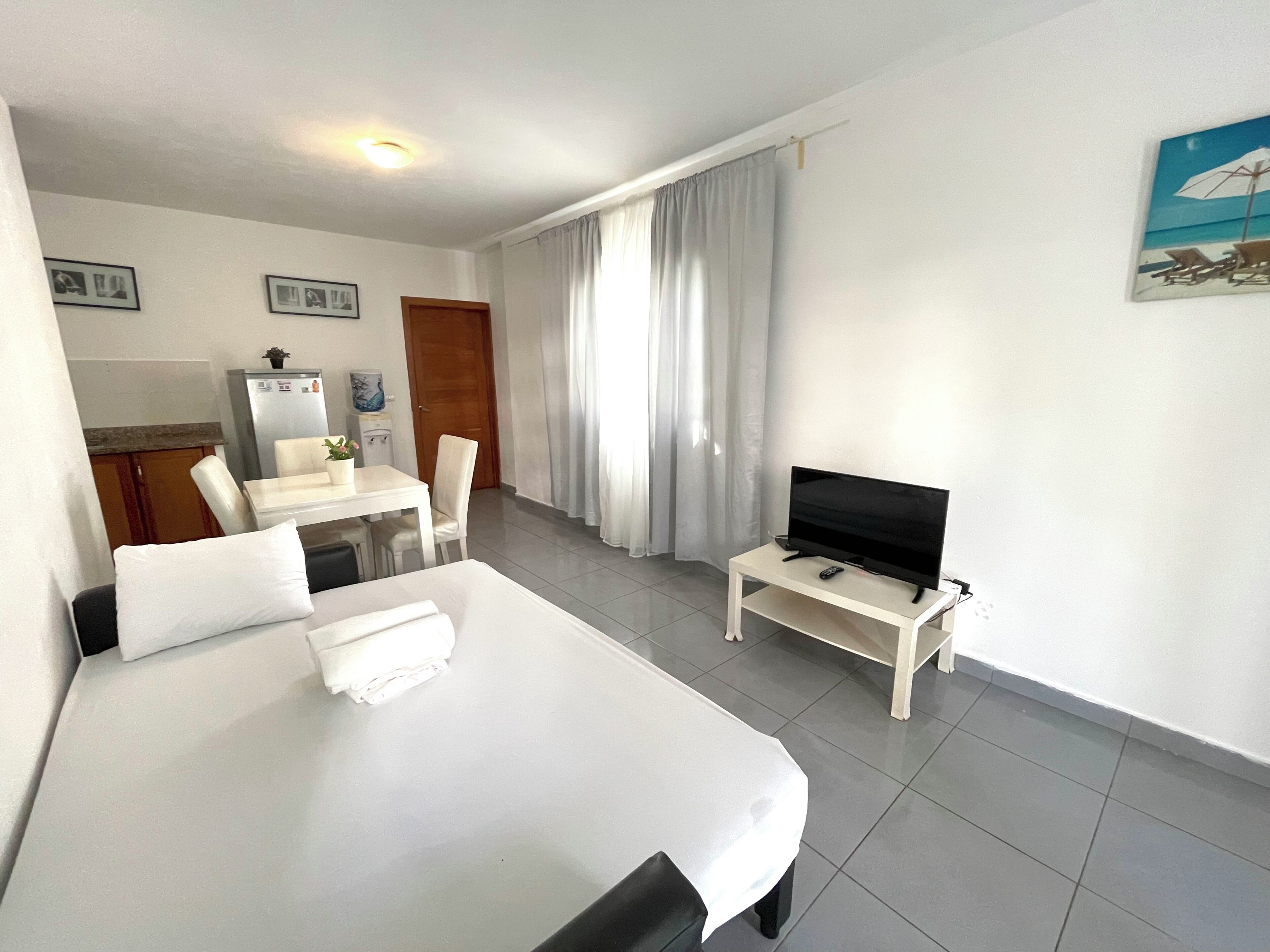 Une chambre d’hôtel avec un lit, un téléviseur posé sur un meuble, un bureau avec une chaise et une fenêtre avec des rideaux.