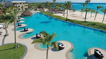 A resort with a large swimming pool, lounge chairs, palm trees, and a beach.