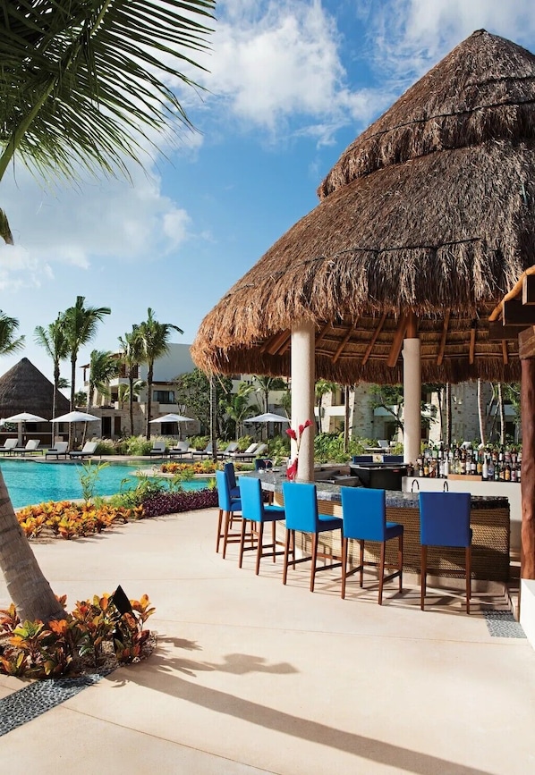 A resort pool area with a thatched umbrella, lounge chairs, and a bar area.