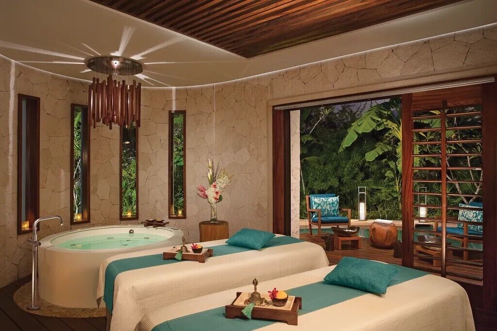 A spa room with two beds, a bathtub, and a view of lush greenery.