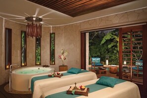 A spa room with two beds, a bathtub, and a view of lush greenery.