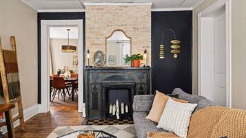 A living room with a fireplace, a sofa, a coffee table, and a dining area in the background.