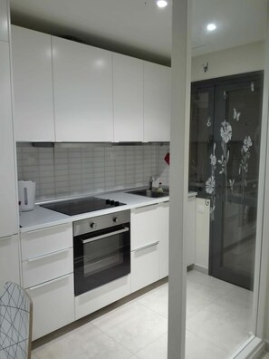A modern kitchen with white cabinets, a black countertop, a built-in oven, and a glass door with floral designs. - Modern Apartment with Pool View—Castillo Caleta de Fuste (Castillo Caleta de Fuste)