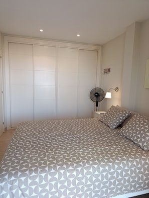 A bedroom with a bed, a nightstand, a wall-mounted fan, and a closet. - Modern Apartment with Pool View—Castillo Caleta de Fuste (Castillo Caleta de Fuste)