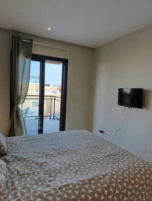 Habitació d'hotel amb un llit, una televisió penjada a la paret i vista al balcó exterior.