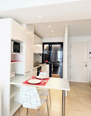 A modern kitchen with white cabinetry, a microwave, and a dining area with a white table and chairs. - Modern Apartment with Pool View—Castillo Caleta de Fuste (Castillo Caleta de Fuste)
