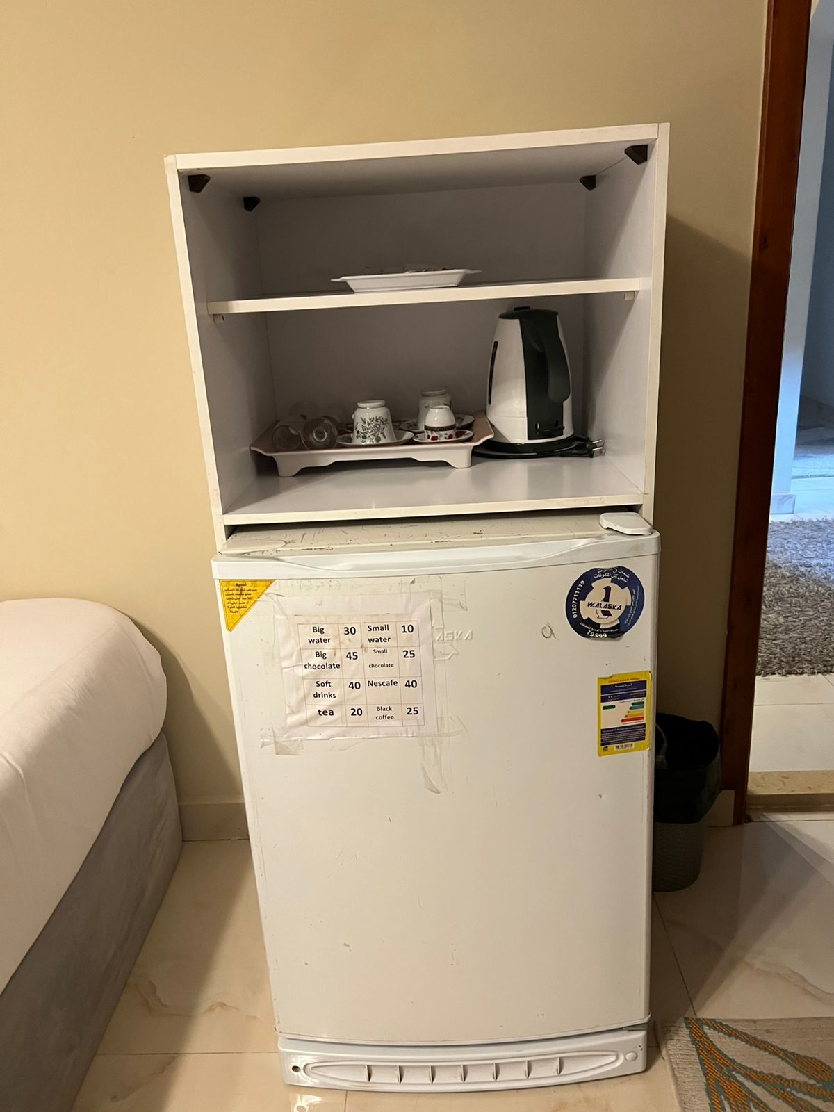 A white refrigerator with a freezer compartment on top, containing a kettle, cups, and a plate.