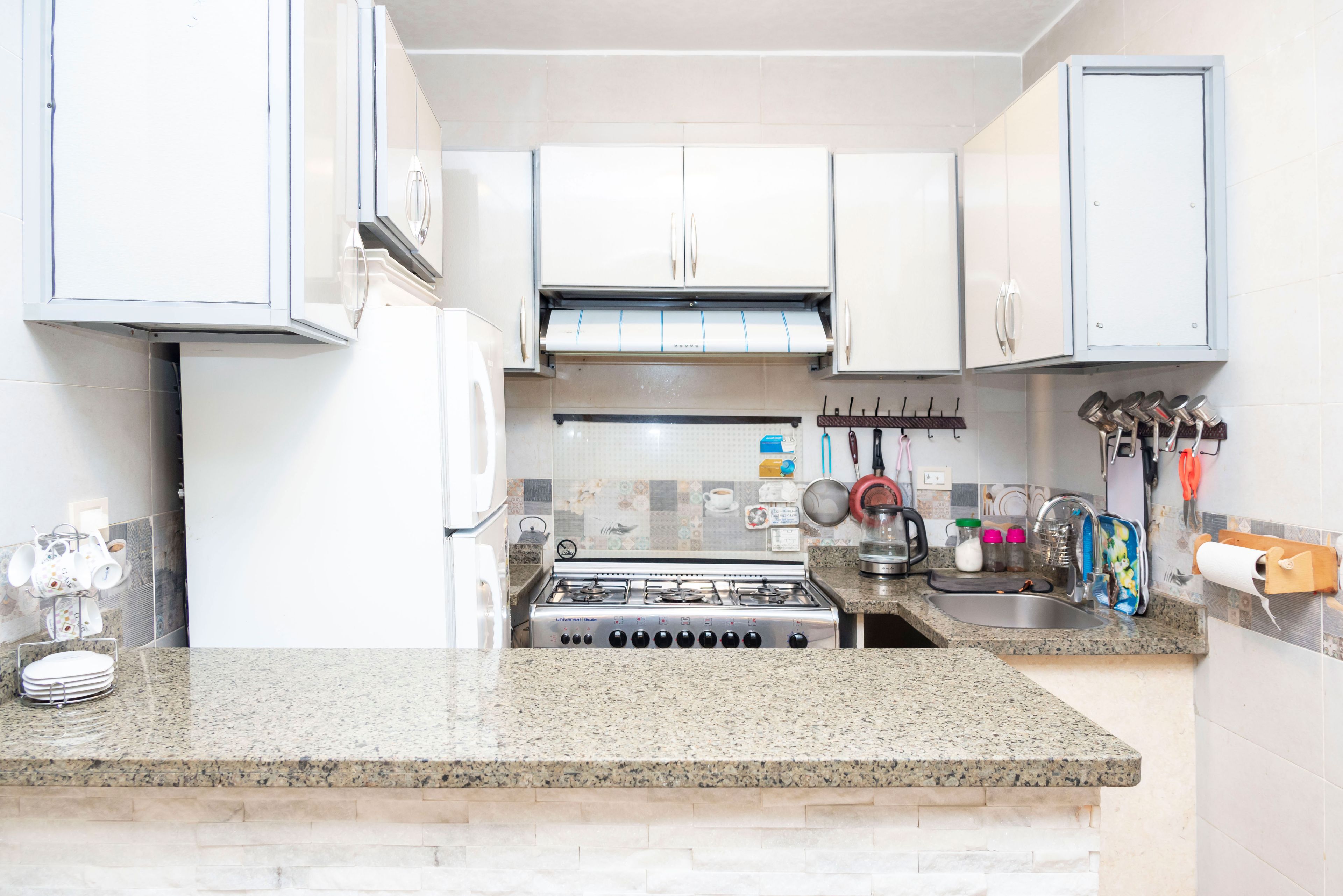 A kitchen with white cabinets, a gas stove, a sink, and various kitchen utensils.
