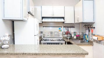 A kitchen with white cabinets, a gas stove, a sink, and various kitchen utensils.