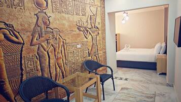 A room with a wall mural of ancient Egyptian hieroglyphs, a bed with white bedding, and a small table with chairs.