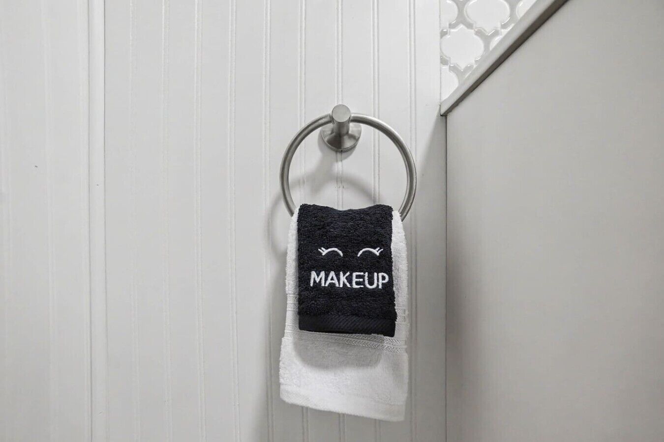 Une serviette ornée d’un motif de maquillage, suspendue à un anneau métallique.