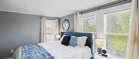 A bedroom with a bed, bedside tables, a clock, and windows with curtains.
