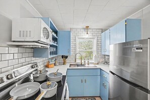 A modern kitchen with blue cabinets, stainless steel appliances, and a window providing natural light.