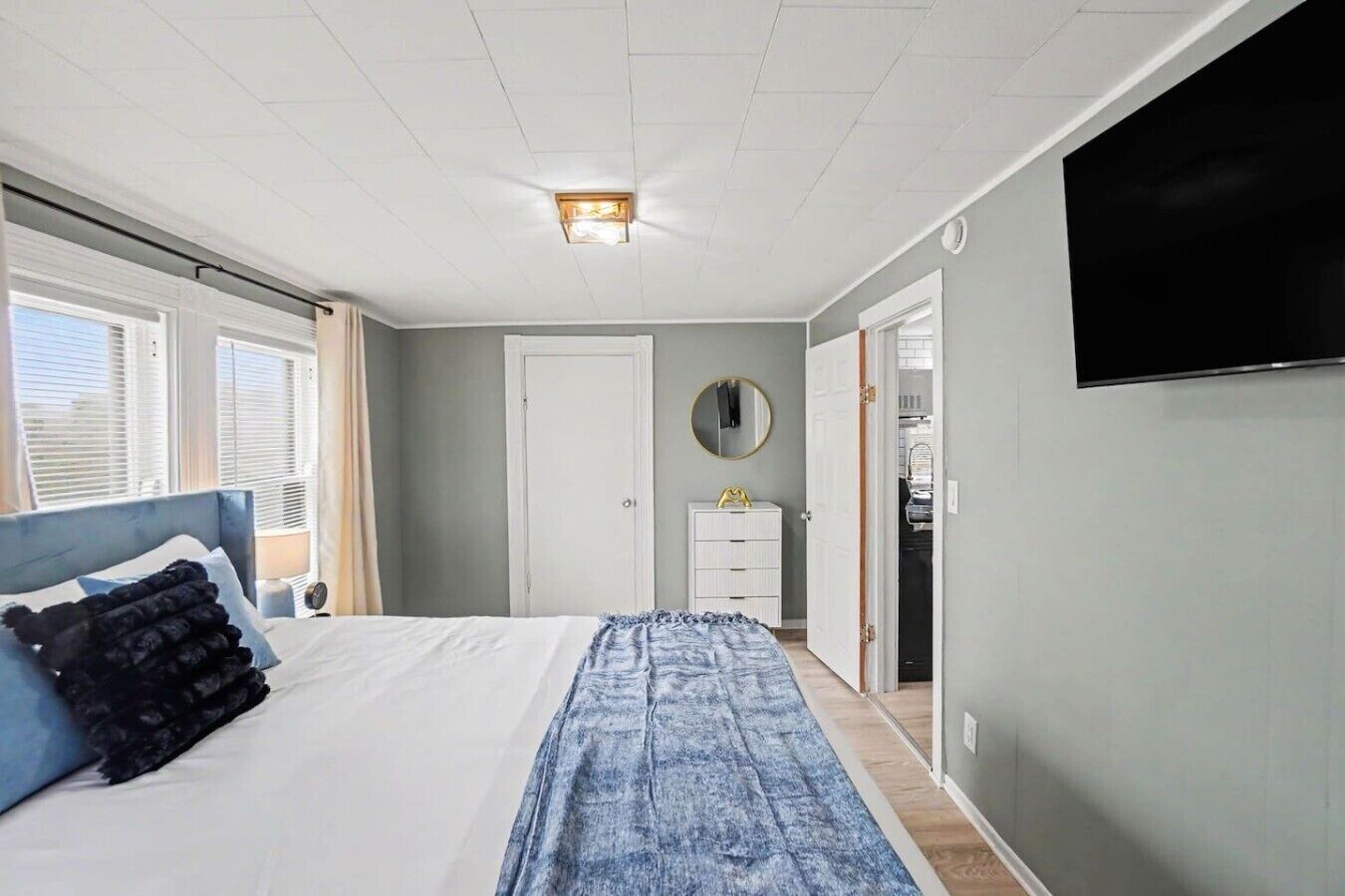 A bedroom with a bed, a dresser, a mirror, a television, and a door leading to a closet.