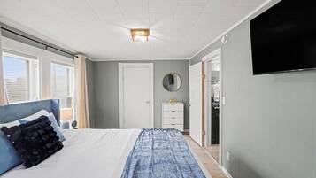 A bedroom with a bed, a dresser, a mirror, a television, and a door leading to a closet.