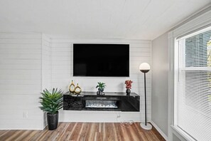 Un salon avec un téléviseur à écran plat fixé au mur, un meuble de rangement noir en dessous et une lampe sur pied à droite.
