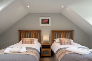 A room with two beds, each with a wooden headboard, a bedside table with a lamp, and a framed picture on the wall. - Hawthorn Brae - A Peaceful Highland Retreat (Pitlochry)
