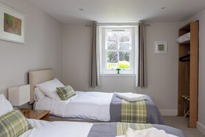 Une chambre avec deux lits, une fenêtre avec des rideaux, une table de chevet avec une lampe et une armoire.