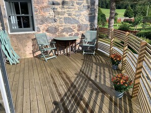 Eine Holzterrasse mit einer Steinmauer, zwei Stühlen, einem Tisch und einem Holzzaun.