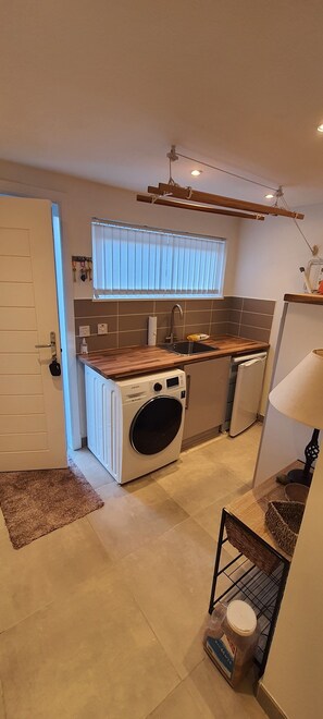 A compact kitchen with a built-in washer, a sink, and a wooden countertop. - Hawthorn Brae - A Peaceful Highland Retreat (Pitlochry)