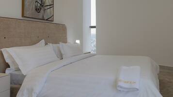 A hotel room with a large bed, white bedding, a headboard, a nightstand, a lamp, and a window with a view.