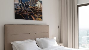 Habitación de hotel con una cama grande, ropa de cama blanca, cabecera, mesita de noche, lámpara, un cuadro y vistas por la ventana.