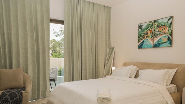 Habitación de hotel con cama, una silla, un cuadro y vistas al exterior.