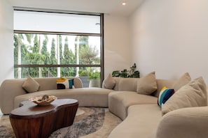 Un salon moderne avec une grande fenêtre, un canapé incurvé, une table basse et une plante.